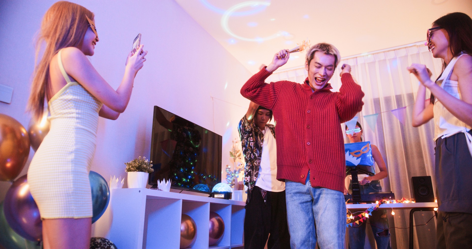 Group of young diverse millennial Asian friends with LGBTQIA+ people dance together at home party, celebrate New Year, Christmas, or Birthday at night. Happy celebration event, fun activity concept